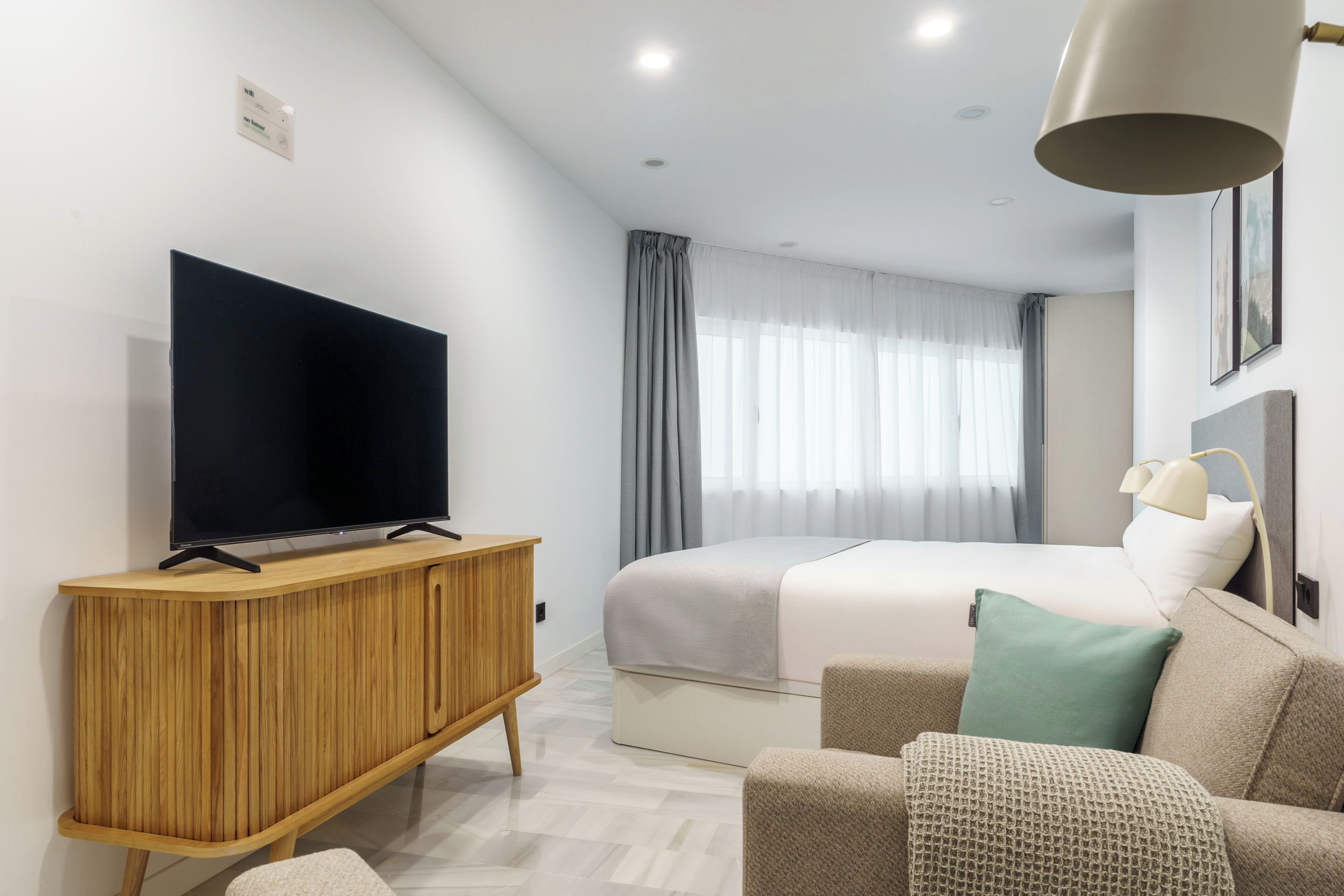 Een moderne hotelkamer met een groot bed, een flatscreen televisie op een houten kast, een bureau en een comfortabele zithoek.
