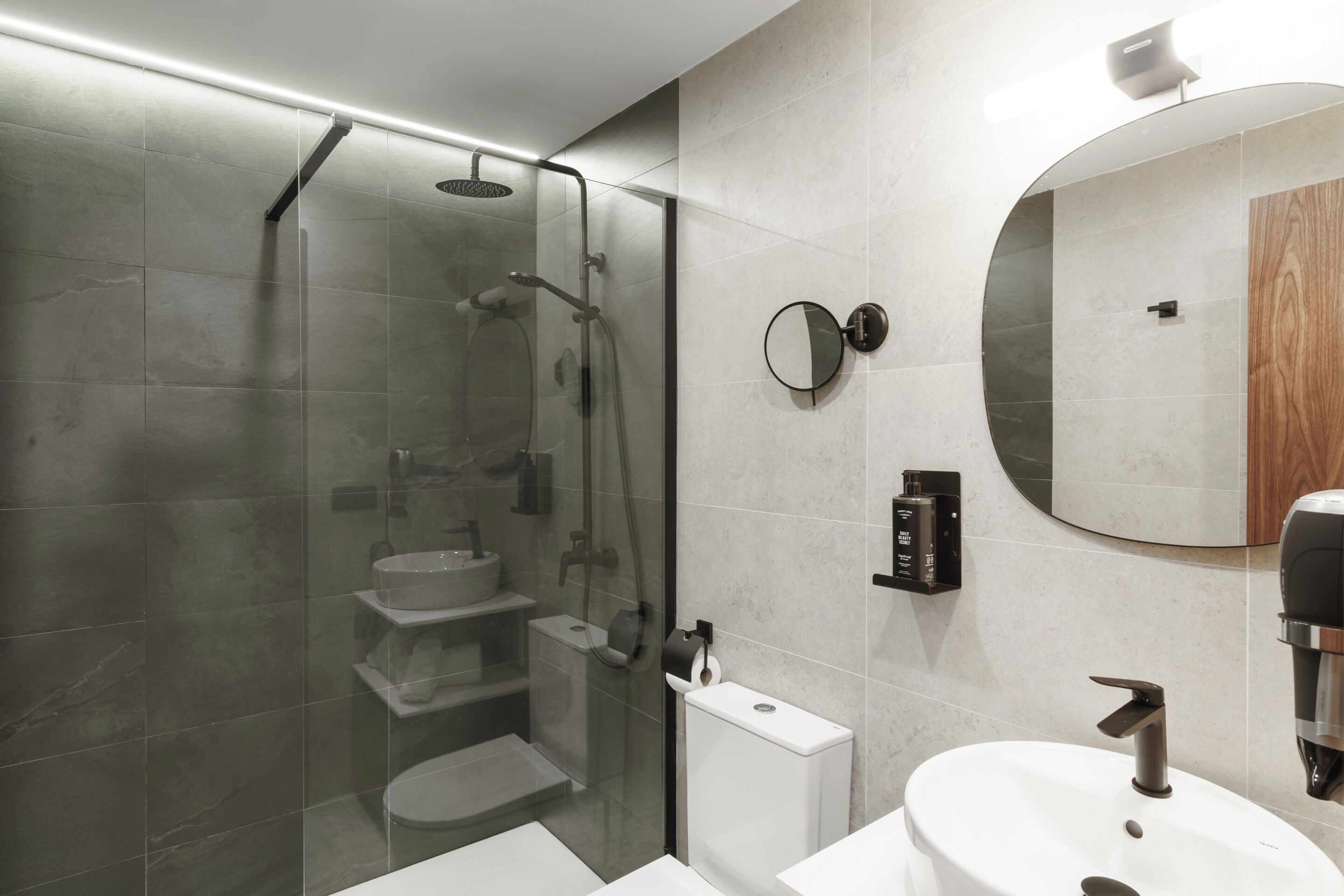 Un bany modern amb dutxa envidriada, un lavabo blanc i un mirall rodó.