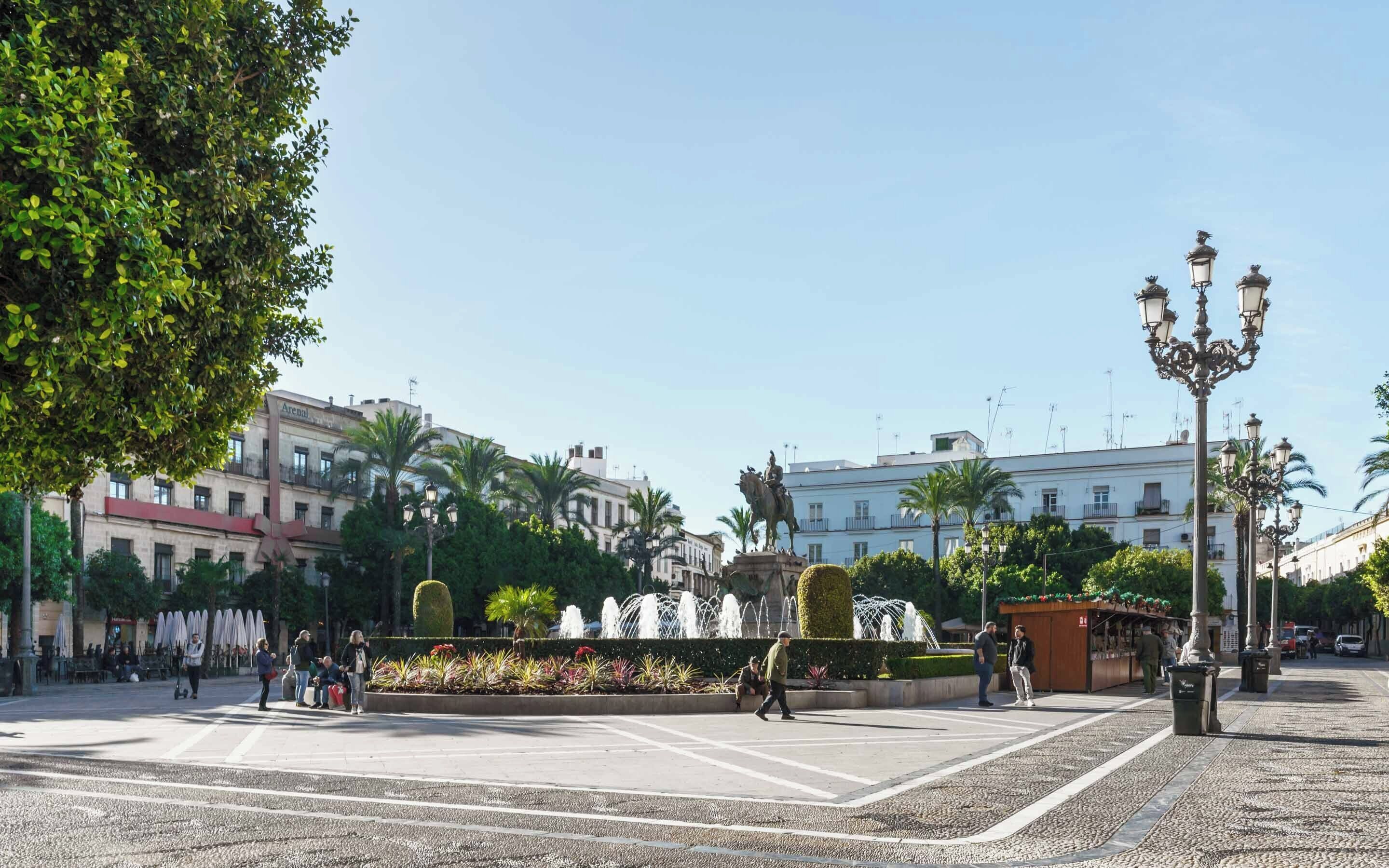 A public square with a fountain, palm trees, and a statue.
