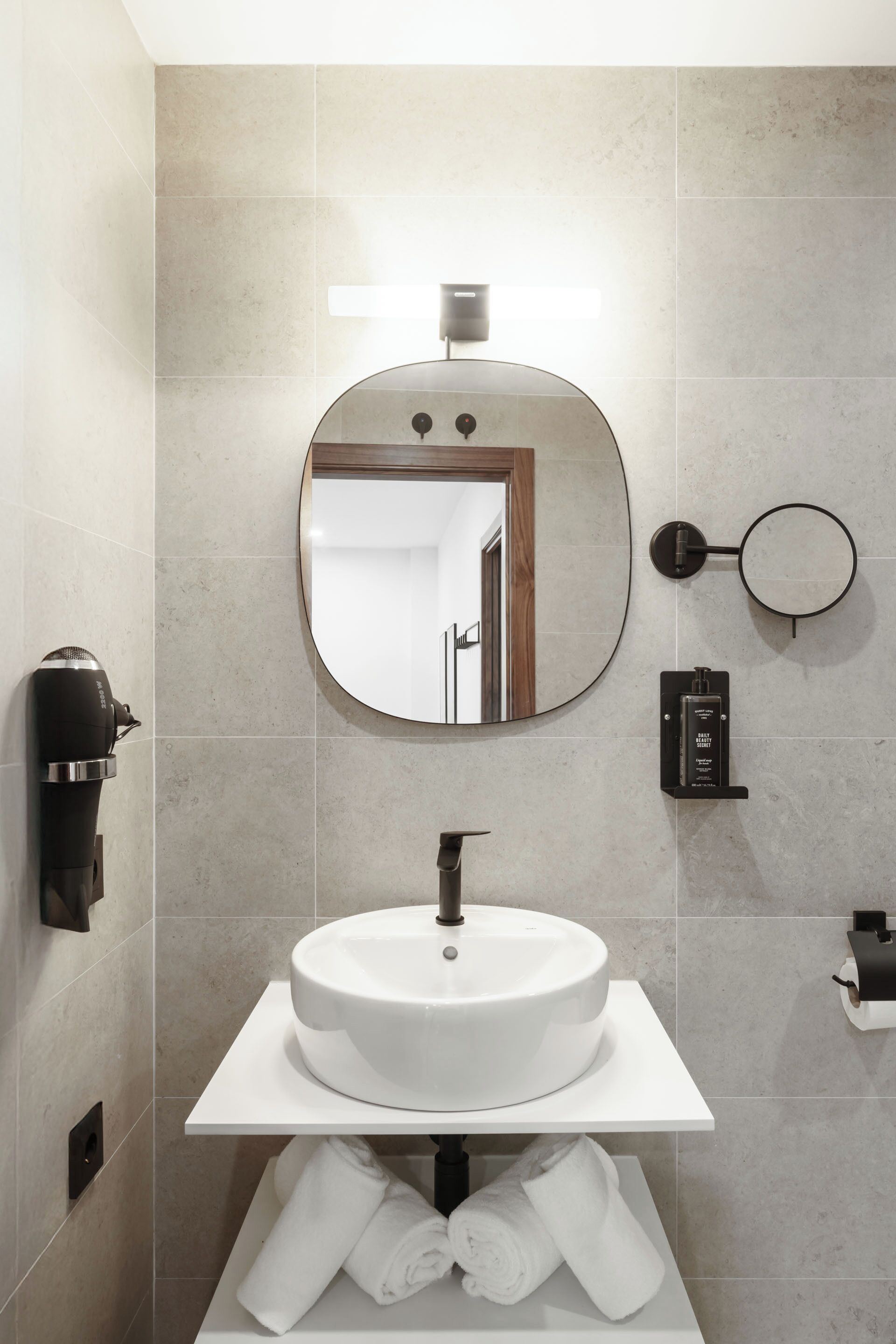 A modern bathroom with a round mirror, a white sink, and a towel rack.