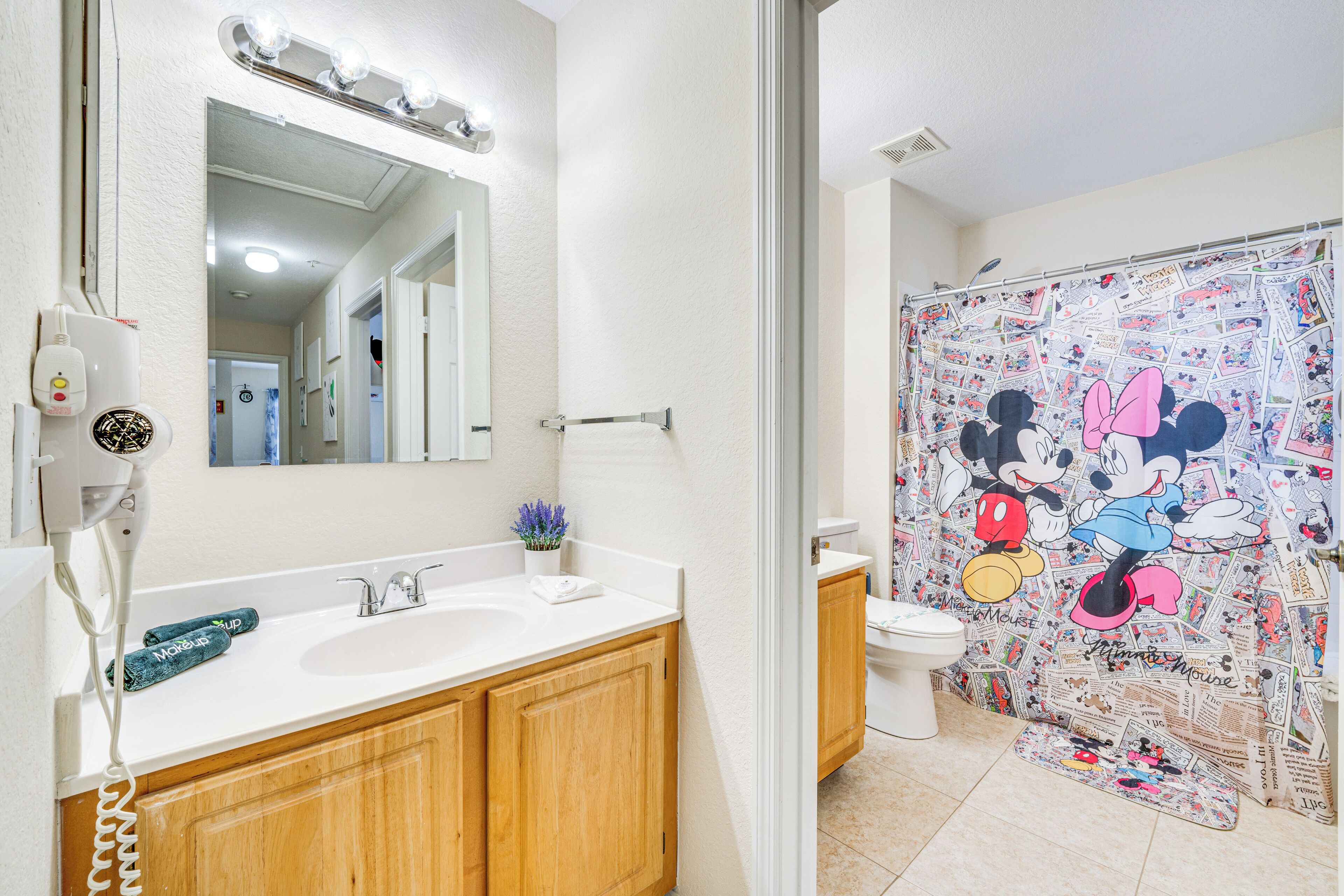 A bathroom with a white sink, wooden cabinets, a mirror, and a Mickey Mouse themed shower curtain.
