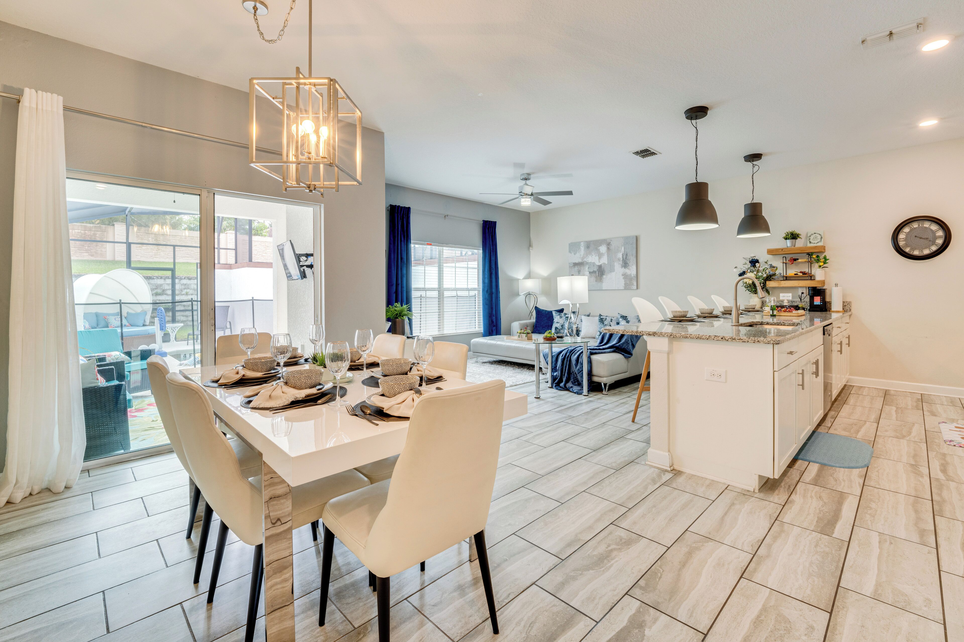 A modern kitchen with a dining area, large windows, and a ceiling fan.