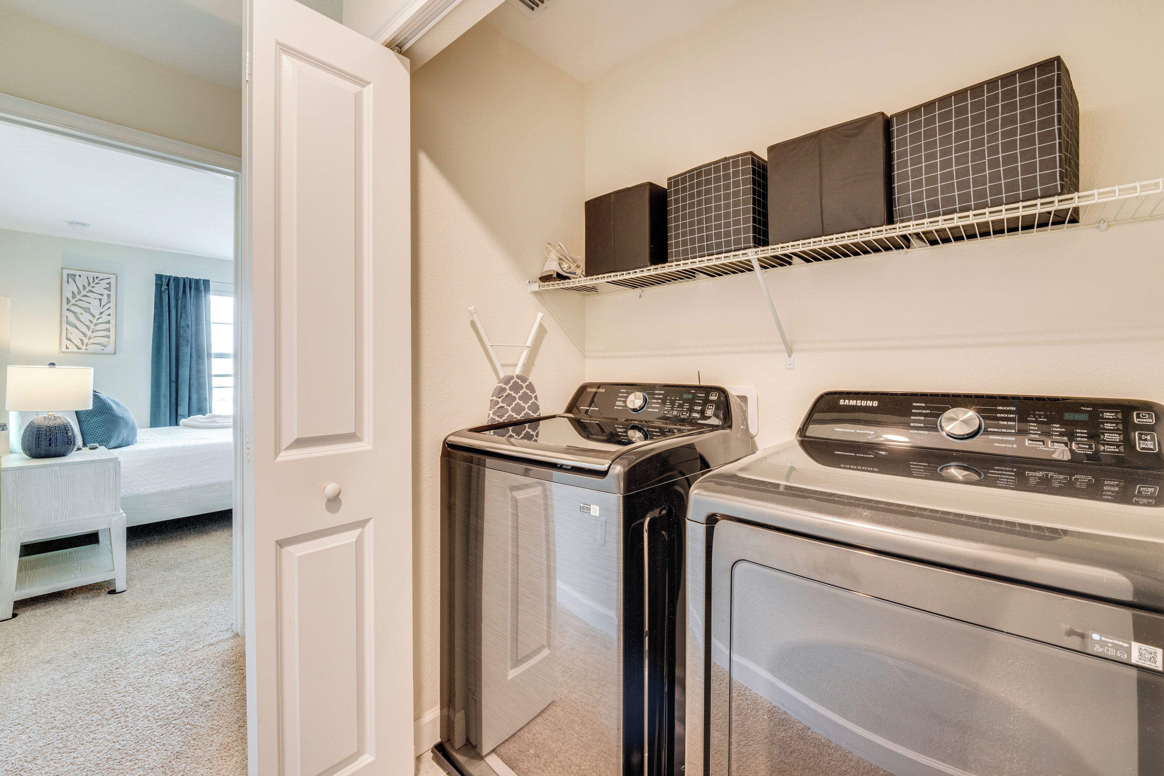 A laundry area with a front-loading washer and dryer, a small table with a lamp, and a shelf above the dryer.
