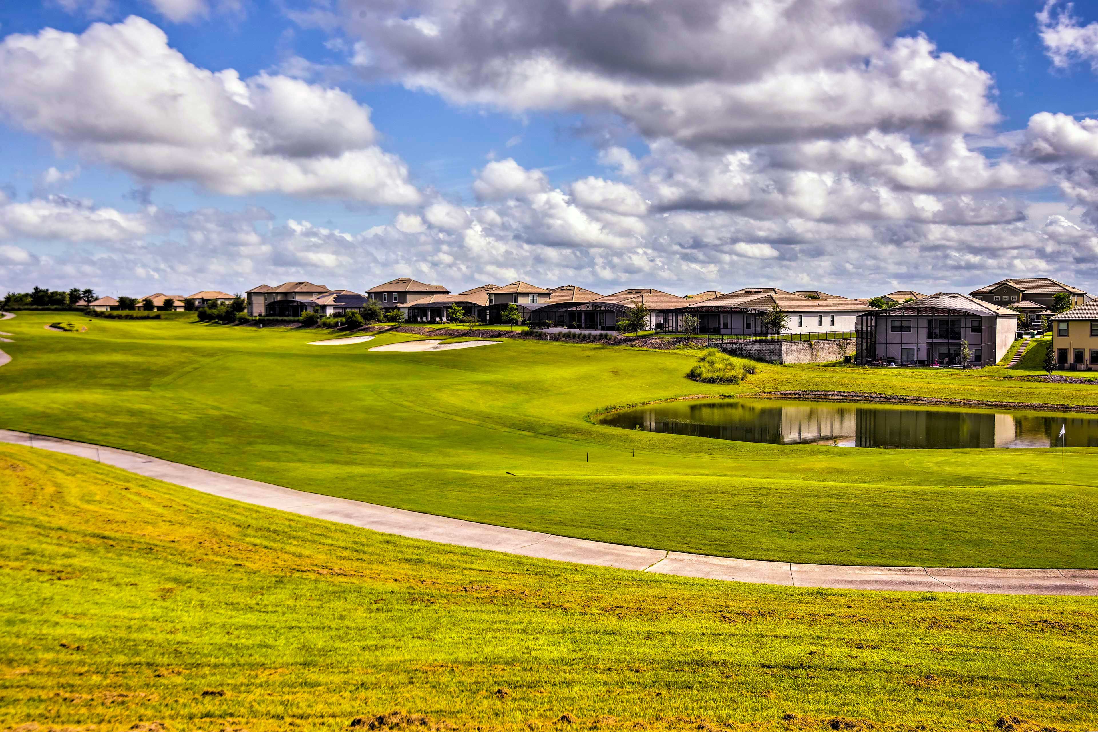 Un terrain de golf avec un étang, des maisons en arrière-plan et un ciel dégagé.