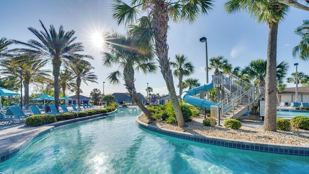 Une piscine bordée de palmiers, avec des chaises longues et un toboggan bleu.