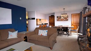 A living room with a sofa, a coffee table, a dining area with a table and chairs, and a kitchen in the background. - The Evergreen. Hot tub, grill, walk to slopes. (Crested Butte)