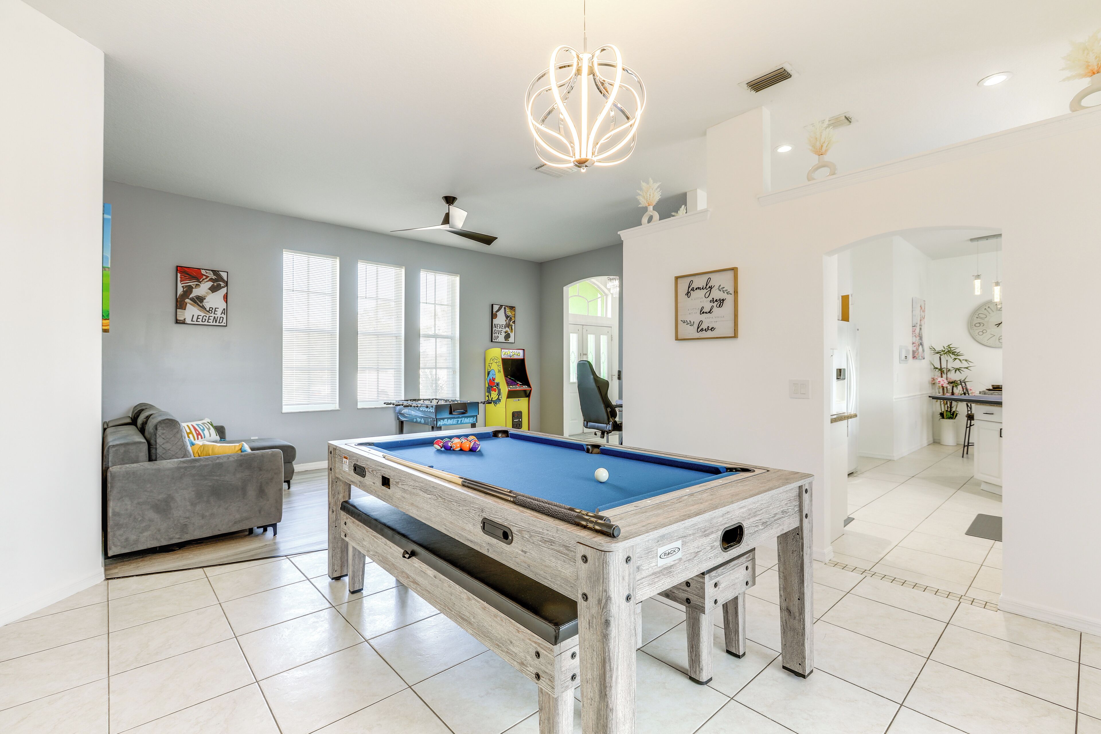 A modern living room with a pool table, grey sofa, and a ceiling fan.