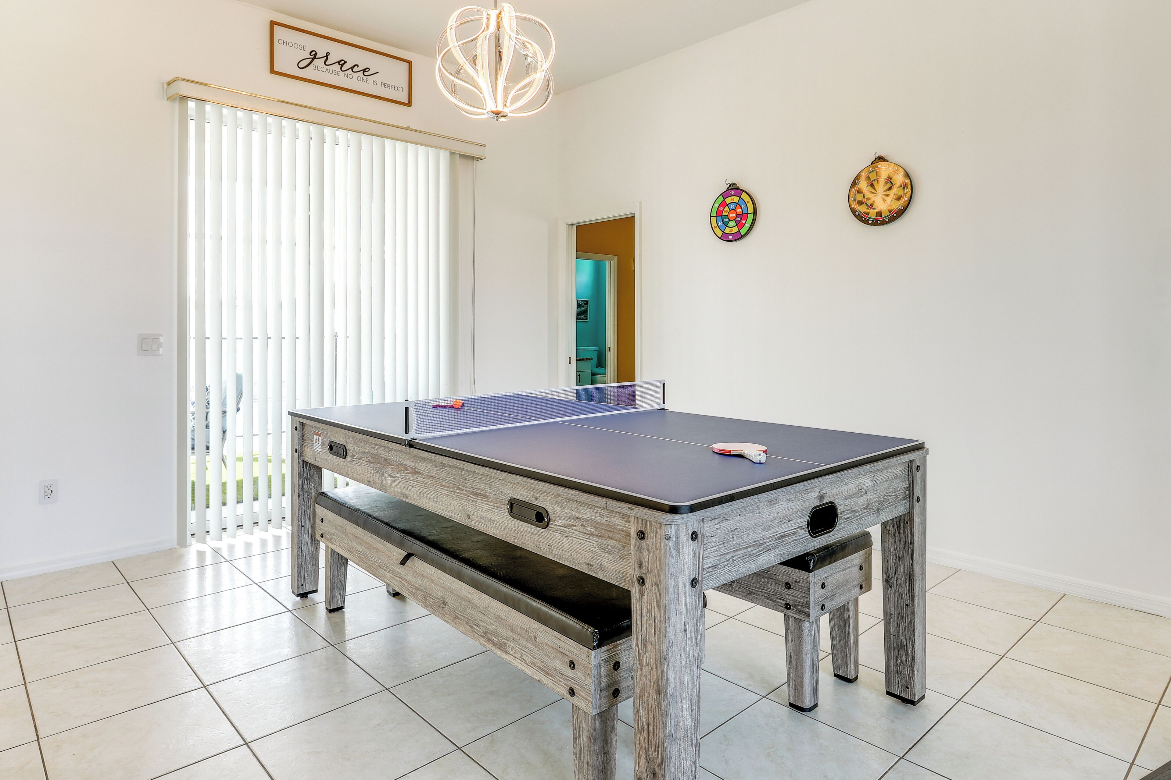A ping pong table in a room with white walls, a wooden bench, and a ceiling light fixture.