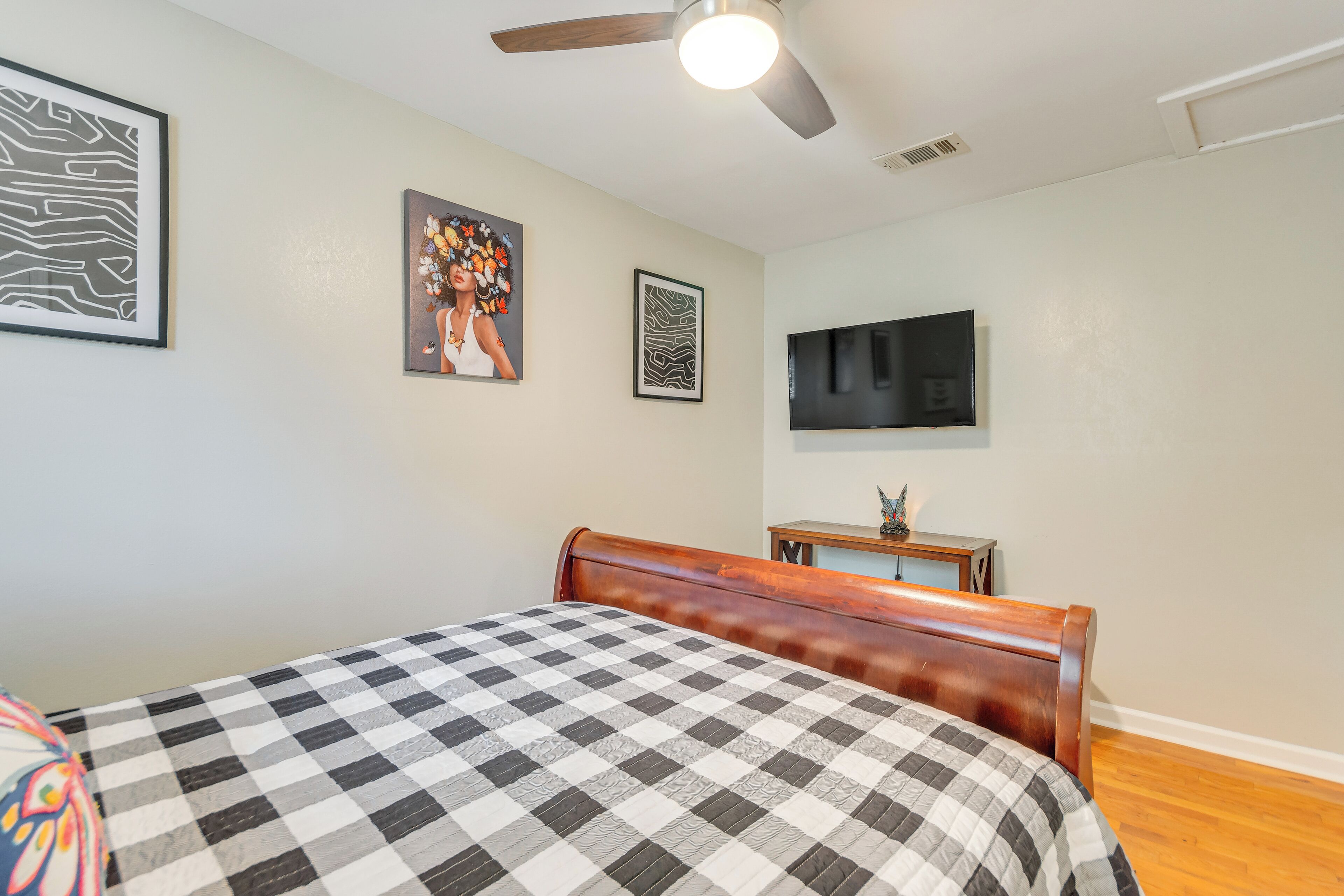 A bedroom with a checkered bedspread, a wooden headboard, a flat-screen TV, and artwork on the walls.