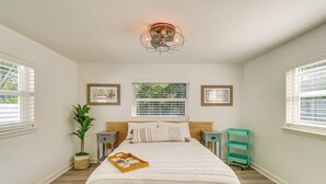 A bedroom with a bed, a ceiling fan, a window with blinds, a bedside table, a nightstand, a potted plant, and a green cart. - 5 Mi to Vero Beach: Vintage Home w/ Sauna & Grill! (Vero Beach)