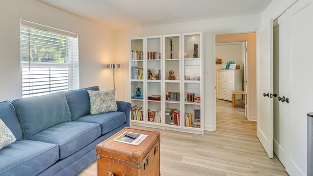 A living room with a blue sofa, a wooden chest, and a bookshelf filled with books and decorative items. - 5 Mi to Vero Beach: Vintage Home w/ Sauna & Grill! (Vero Beach)