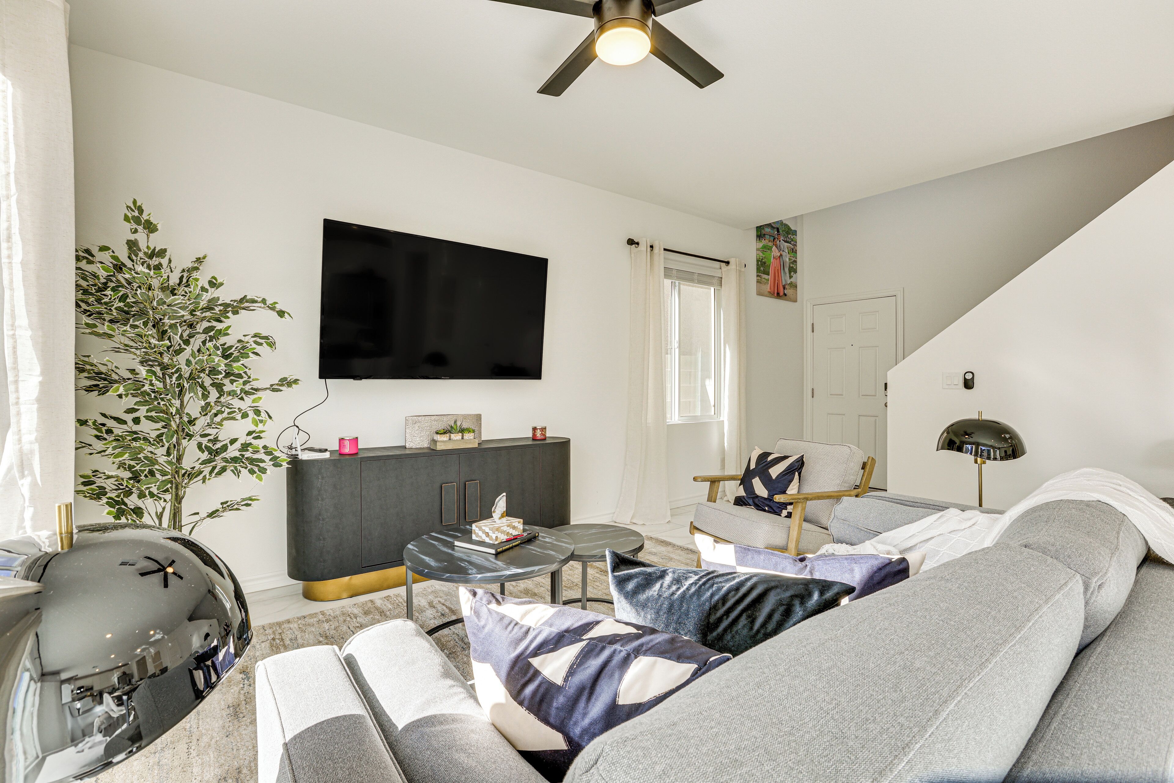 A modern living room with a grey sofa, a black entertainment unit, a flat-screen TV, and a ceiling fan.