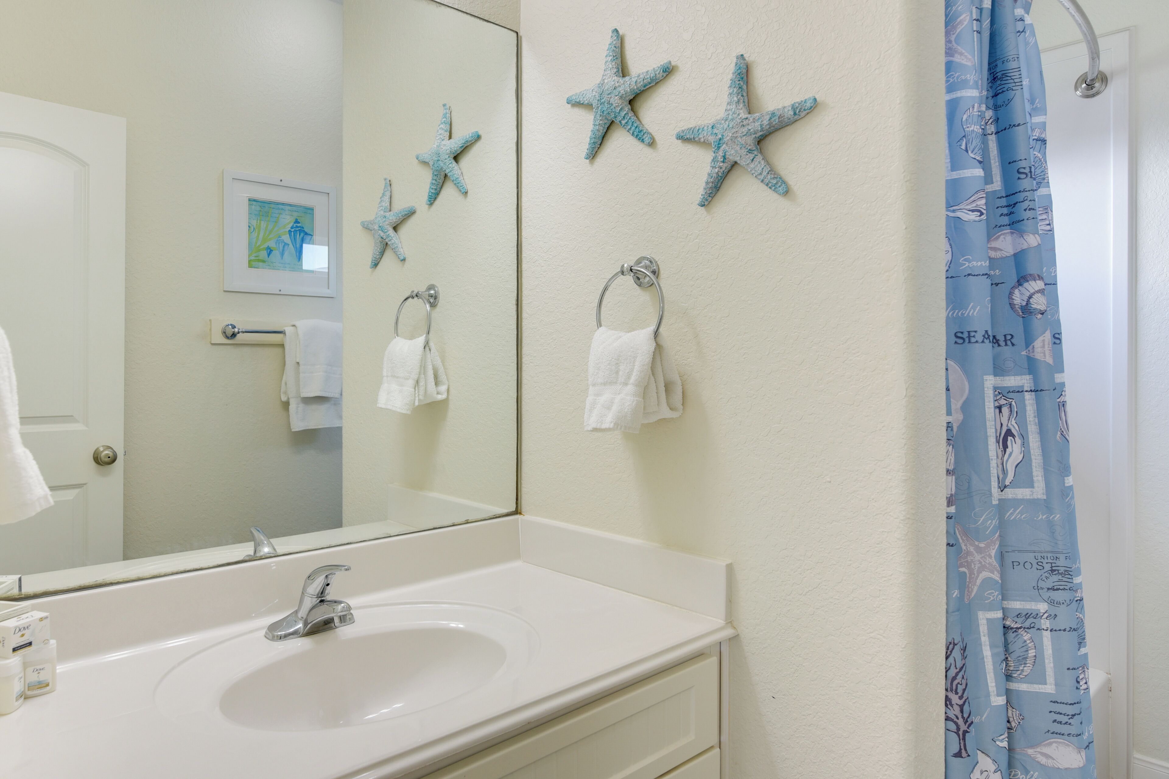 A bathroom with a white sink, a mirror, and starfish decorations on the wall.