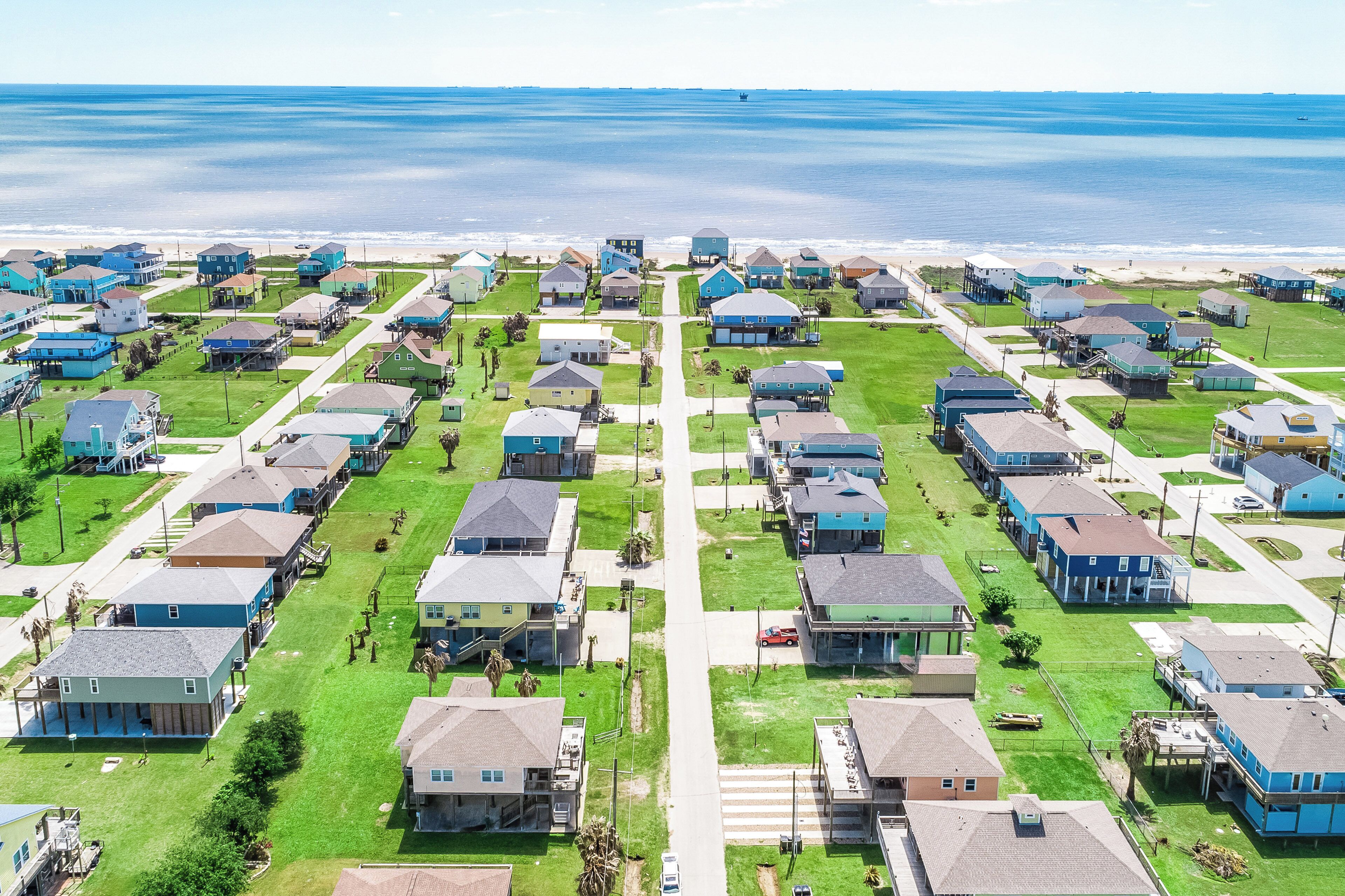 Un quartier résidentiel situé sur la côte, où les maisons sont alignées en rangées le long de la plage, avec de belles pelouses verdoyantes et une vue dégagée sur l’océan.
