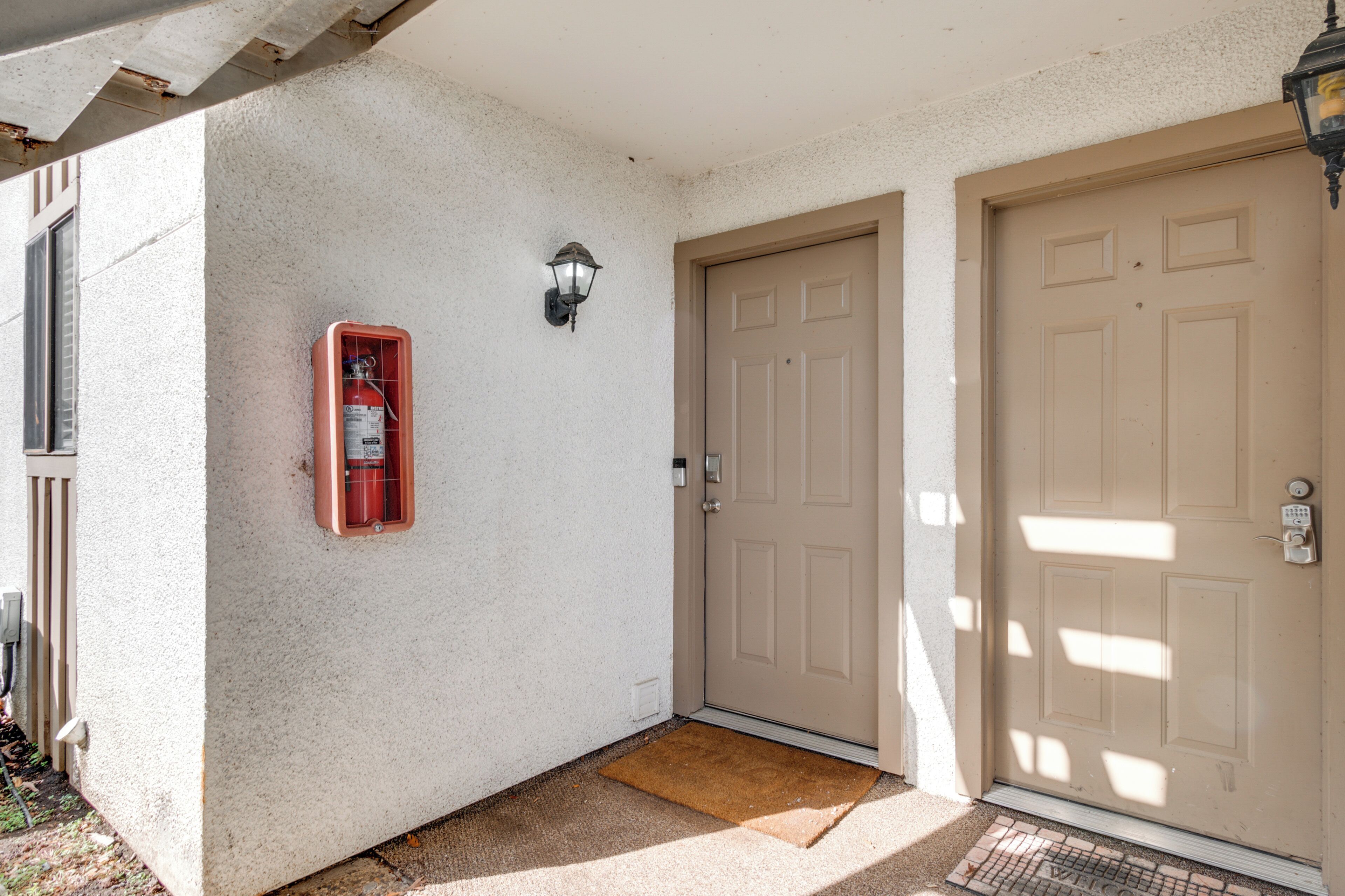 Eine beige Tür mit einem Briefschlitz und einem roten Feuerlöscher an der Wand.