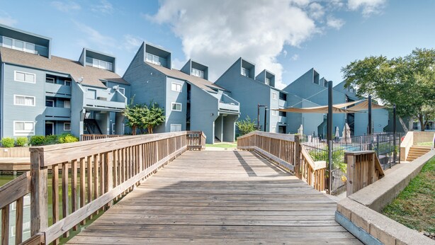 A wooden boardwalk leading to a row of blue apartment buildings with balconies and a clear sky.