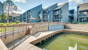 A modern building with multiple balconies and a wooden deck over a pond.