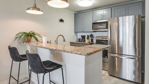 A modern kitchen with granite countertops, stainless steel appliances, and pendant lighting.