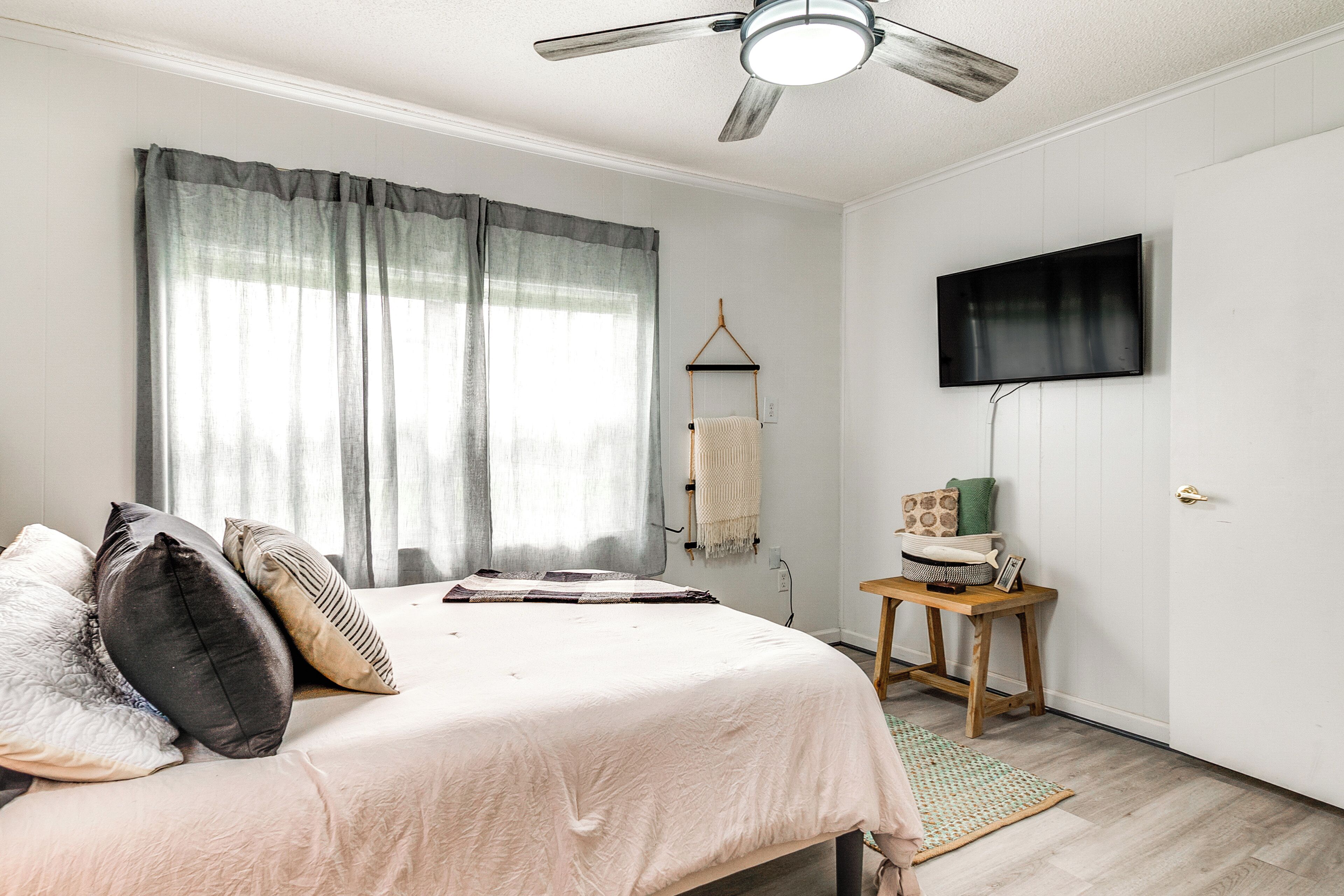 A bedroom with a bed, a ceiling fan, a TV mounted on the wall, and a small wooden table.