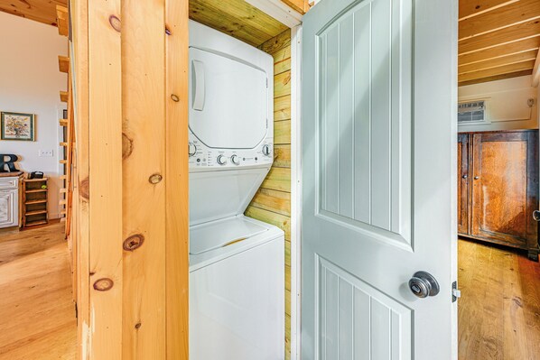 A laundry room with a white washer and dryer, wooden walls, and a white door. - Deck & Fire Pit: Mtn-view Cabin in Rabun Gap (Mountain City)