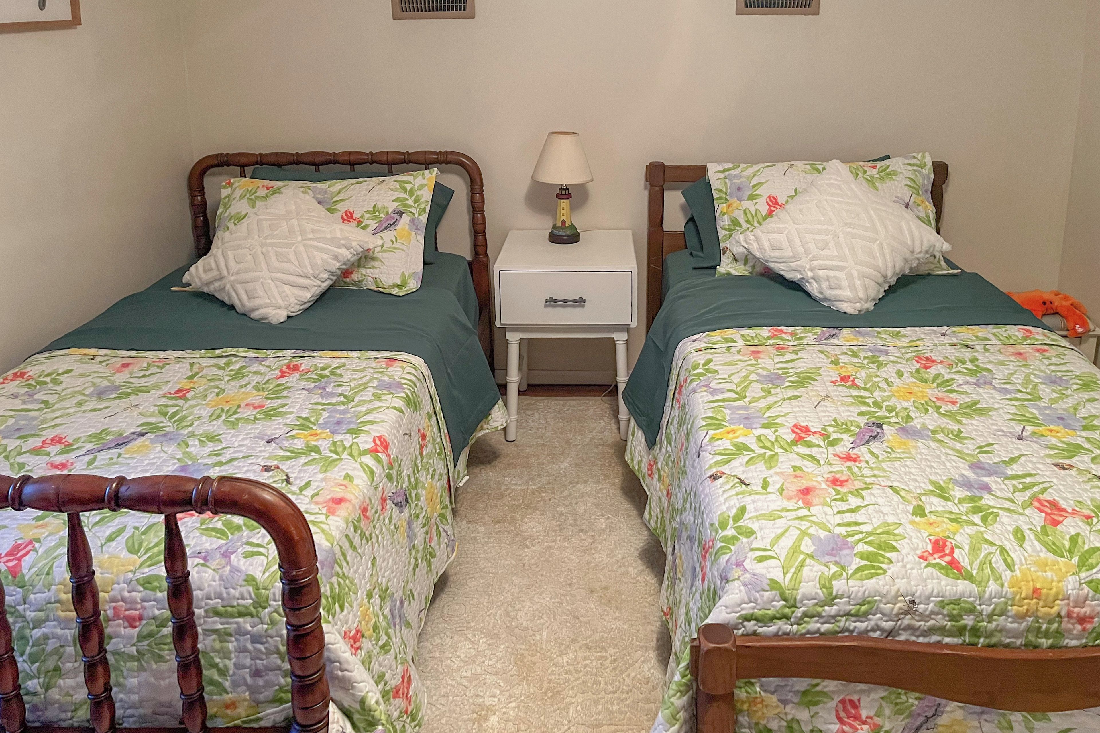 A twin bedroom with two beds, each with floral bedding, a nightstand with a lamp, and a wooden chair.