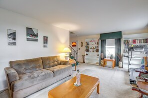 Una sala de estar con sofá, mesa de centro y lámpara. Se ve una escalera que lleva a otra habitación.
