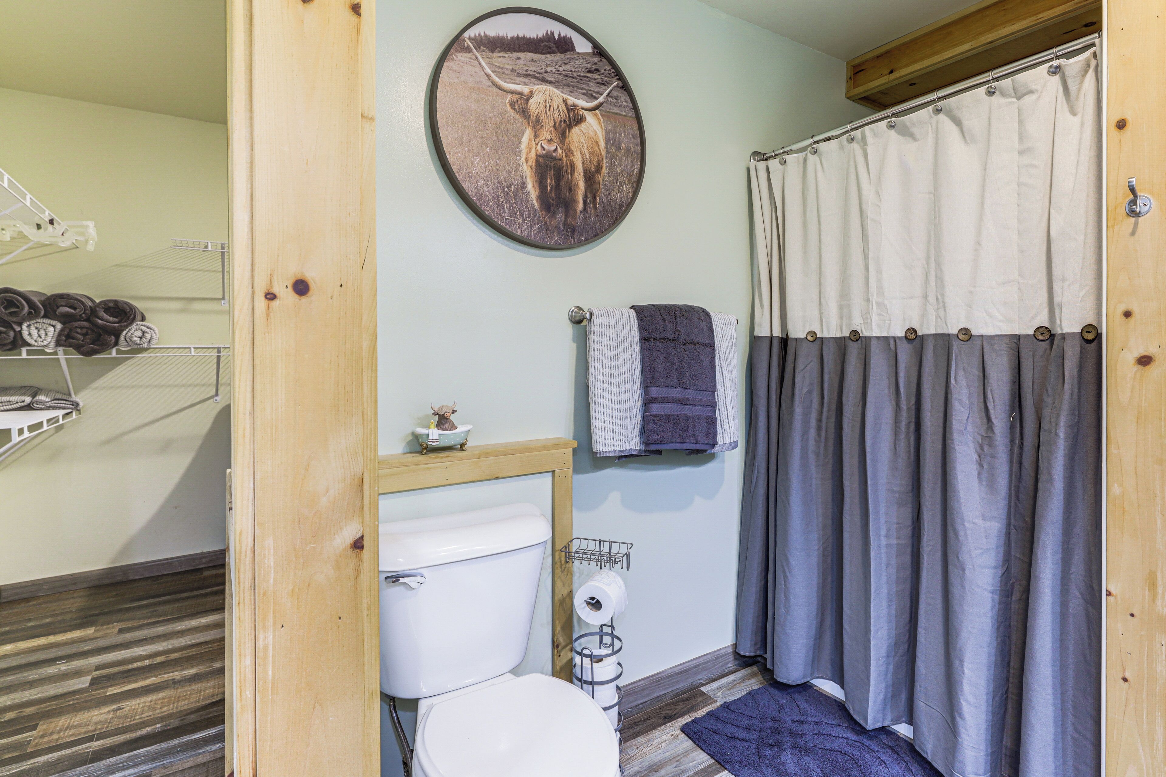 Une salle de bain équipée de toilettes, d’un porte-serviettes, d’un rideau de douche et d’un tableau représentant un taureau accroché au mur.