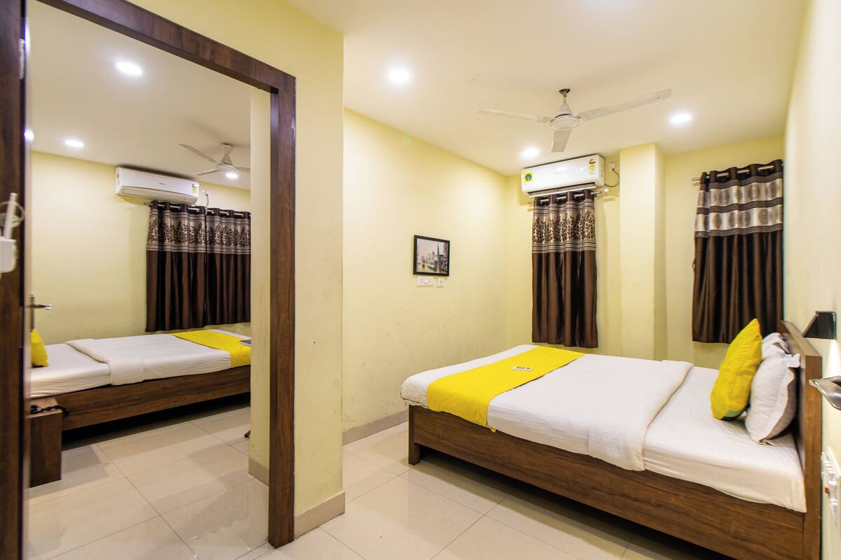 Habitación de hotel con dos camas, ventilador de techo, unidad de aire acondicionado y un espejo que refleja la habitación.