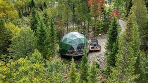 Struttura a cupola geodetica in una zona boschiva, con una terrazza e posti a sedere all'aperto.