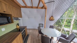Una cucina moderna con mobili in legno, un forno a microonde integrato e un piano cottura. C'è un'area pranzo con un tavolo rotondo e quattro sedie. La stanza ha ampie finestre che offrono vista su alberi e un ruscello.
