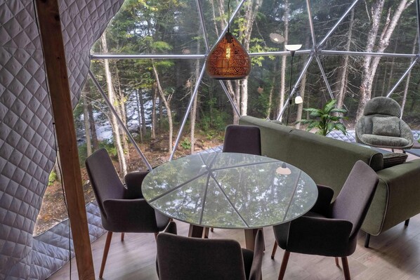 A modern interior with a round glass table, black chairs, a green sofa, and a hanging light fixture.