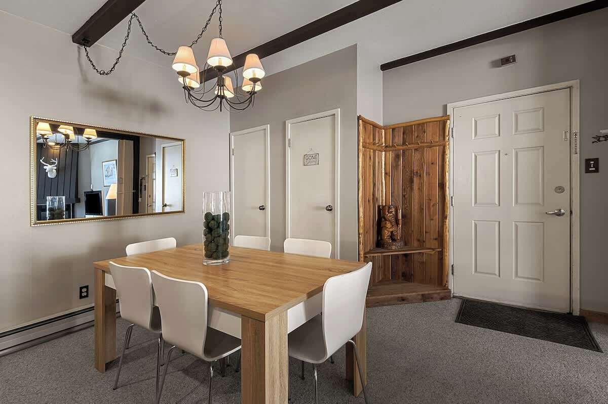 Un coin repas avec une table en bois, des chaises blanches, un lustre et un miroir au mur.