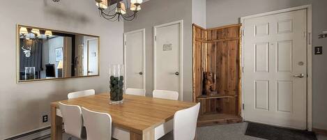Un coin repas avec une table en bois, des chaises blanches, un lustre et un miroir au mur.