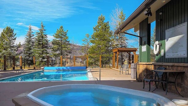 Un área de piscina con jacuzzi, mobiliario exterior y una pérgola de madera.