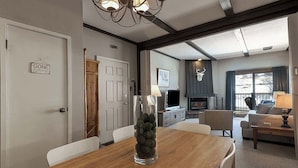 Un comedor con una mesa y sillas de madera, un florero transparente con piedras decorativas, un televisor y una chimenea al fondo.