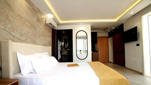 Une chambre d’hôtel moderne avec un grand lit, une table de chevet en bois, un miroir et un téléviseur fixé au mur.