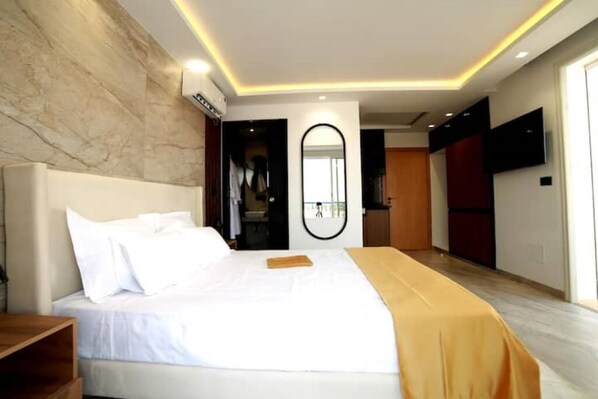 Ein modernes Hotelzimmer mit einem großen Bett, einem Nachttisch aus Holz, einem Spiegel und einem an der Wand befestigten Fernseher.