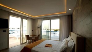 Une chambre d’hôtel avec un grand lit, un balcon avec vue et une petite table avec des chaises.
