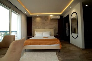 Ein modernes Schlafzimmer mit einem großen Bett, einem Sessel, Balkonblick und einem Spiegel.