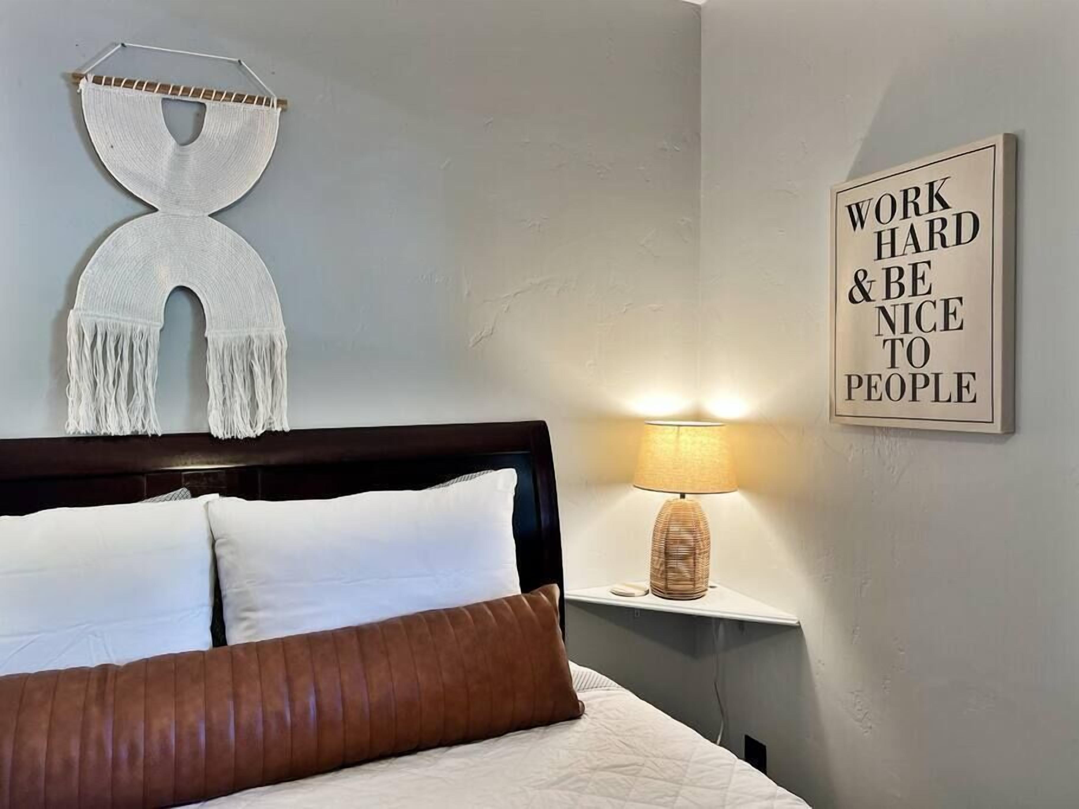 Een slaapkamer met een bed, een wandlamp en een motiverende quote op de muur.