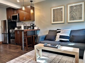 A modern kitchen with dark wood cabinets, a stainless steel refrigerator, and a built-in oven. There is a bar stool and a coffee maker on the counter. A gray sofa with striped pillows is against the wall, and two framed artworks are hung above it. - Yampa Valley Viewhaus (Steamboat Springs)
