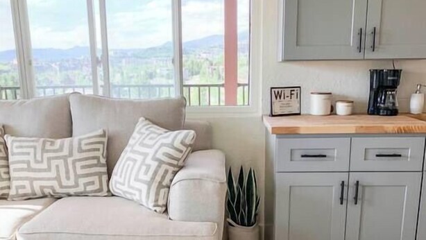 A living room with a sofa, a coffee table, a kitchen area with cabinets and a countertop, and a view through large windows. - Scenic Mountainside Studio (Steamboat Springs)