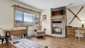 A cozy living room with a stone fireplace, a dining table, and a comfortable armchair. - Gondola Village Chalet (Steamboat Springs)