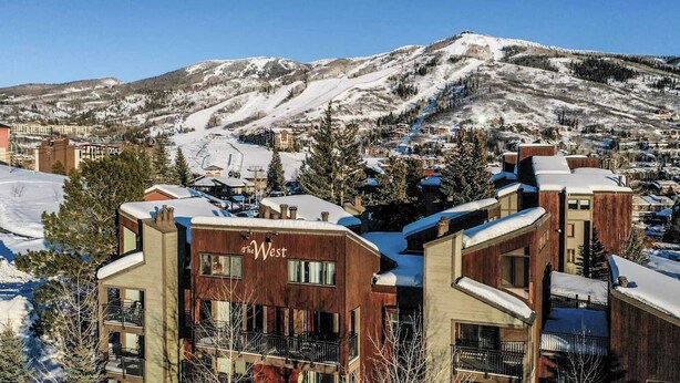 A modern hotel with a wooden facade and balconies, set against a snowy mountain backdrop. - Gondola Village Chalet (Steamboat Springs)
