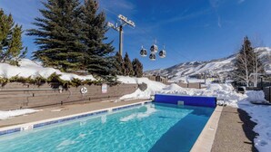 A pool with clear blue water, surrounded by snow and trees, with a ski lift in the background. - Gondola Village Chalet (Steamboat Springs)