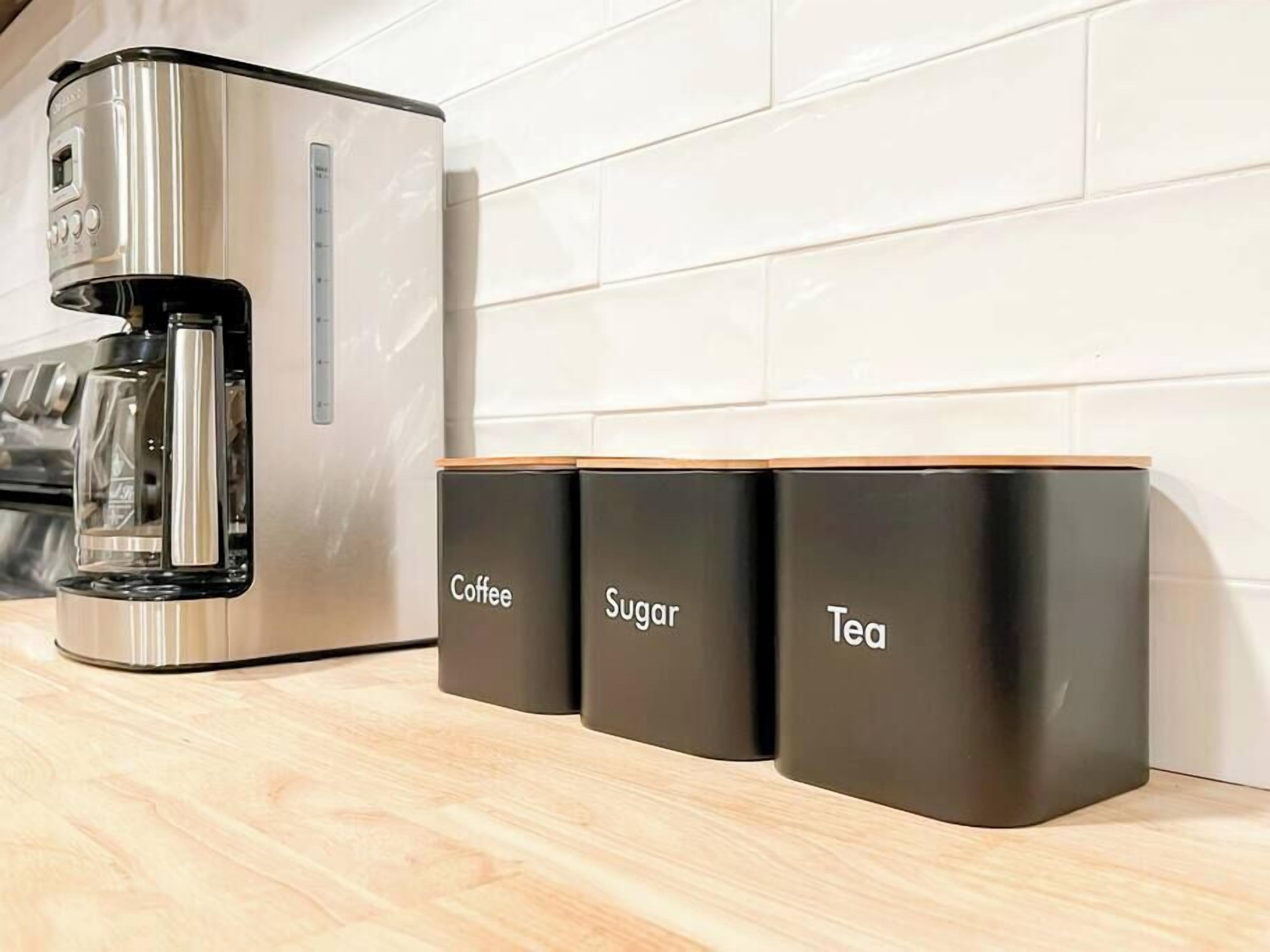 A modern kitchen with a coffee maker and three labeled containers for coffee, sugar, and tea.
