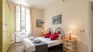 Ein Schlafzimmer mit einem Bett, zwei Nachttischlampen, einem Vorhangfenster, einer Tür und einem gemusterten Boden.
