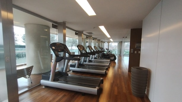 Une salle de sport équipée de tapis de course, dotée d’un plancher en bois et de grandes fenêtres.