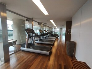 A gym with treadmills, a wooden floor, and large windows.