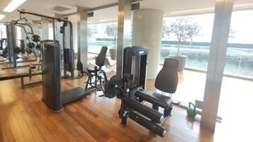 A gym with various exercise equipment, large windows, and a view of a body of water.
